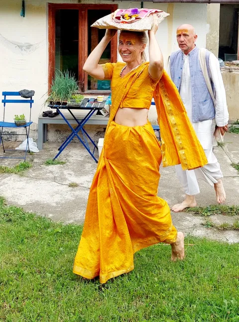 Kobieta w żółtym sari niosąca ofiary podczas procesji Aarti